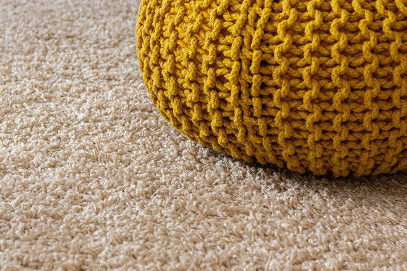 Carpete claro com pufe de tricô amarelo